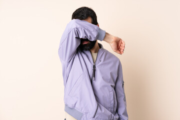 Caucasian man with beard wearing a jacket over isolated background covering eyes by hands