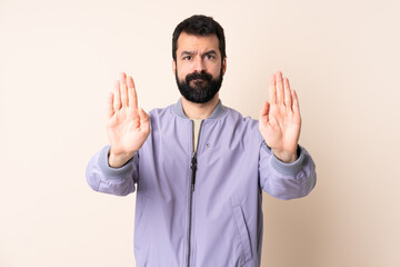 Caucasian man with beard wearing a jacket over isolated background making stop gesture and disappointed