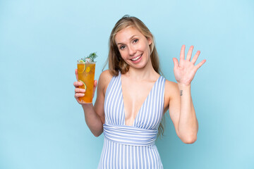 Young blonde woman wearing swimsuit holding a cocktail isolated on blue background saluting with...