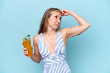Young blonde woman wearing swimsuit holding a cocktail isolated on blue background having doubts...