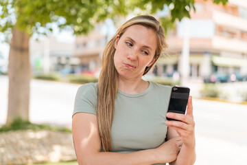 Young blonde woman using mobile phone at outdoors with sad expression