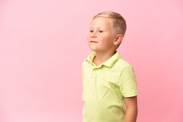 Little Russian boy isolated on pink background looking up while smiling