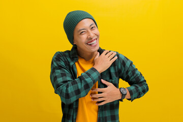 Grateful young Asian man, dressed in a beanie hat and casual clothes, expresses gratitude by...