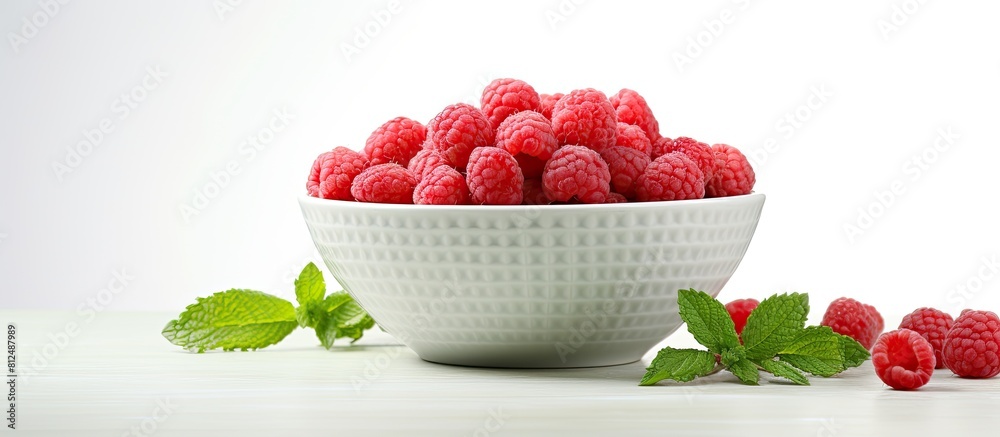 Poster a closeup copy space image of a bowl containing fresh raspberries and mint leaves placed on a light 