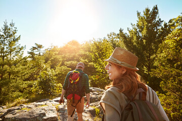 Nature, hiking and couple with sunshine, blue sky and adventure holiday in mountain from back. Trekking, man and woman on travel vacation together in park with trees, bush and outdoor climbing date