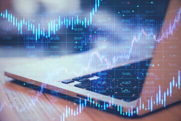 Close up of laptop computer with creative candlestick forex chart with index on blurry background. Trade, finance and stock exchange concept. Double exposure.