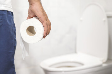 Man suffers from diarrhea hand hold tissue paper roll in front of toilet bowl. constipation in...