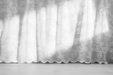 A close-up view of white lace curtains with delicate patterns, hanging in a room. Abstract home...