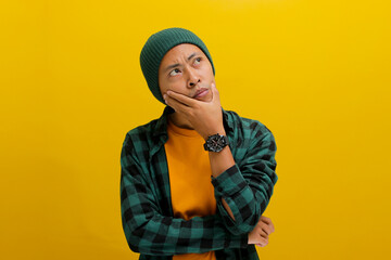 Thoughtful young Asian man, wearing a beanie hat and casual shirt, rests his hand on his chin,...