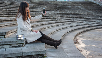 Female Asian tourist wearing a coach shirt sits on the stairs holding a smartphone and taking a...
