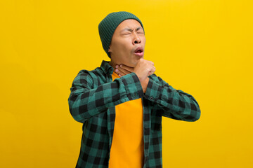 Young Asian man, wearing a beanie hat and casual shirt, appears to be experiencing throat pain and...