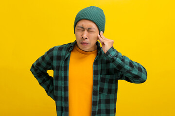 Young Asian man, dressed in a beanie hat and casual shirt, appears to be suffering from otitis and...