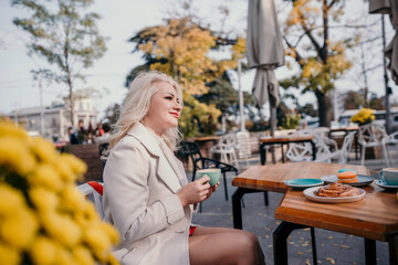 A woman is sitting at a table with a cup of coffee and a pastry. She is smiling and enjoying her time.