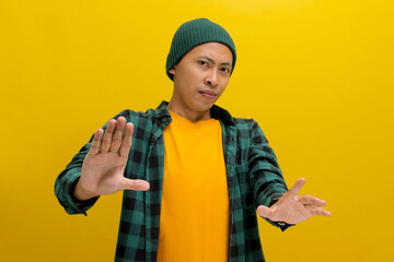 An afraid young Asian man, dressed in a beanie hat and casual shirt, is pulling his hands away with...
