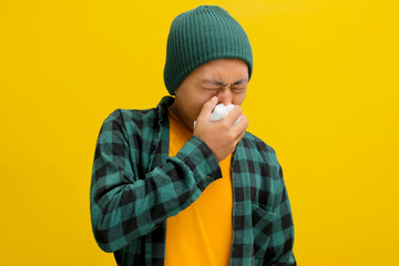 Young Asian man is sneezing and blowing his nose into a napkin, showing signs of suffering from a...