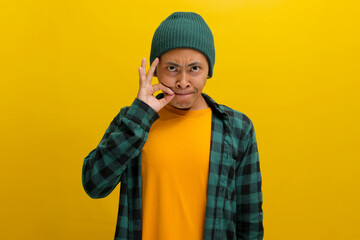 an Asian man, dressed in a casual shirt and wearing a beanie hat, is gesturing for silence by...