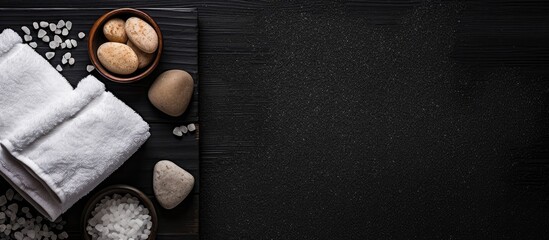 Obraz na płótnie Canvas Top view of a spa set arrangement on a black background featuring sea salt a towel and a pumice stone for foot care The image provides ample copy space for text