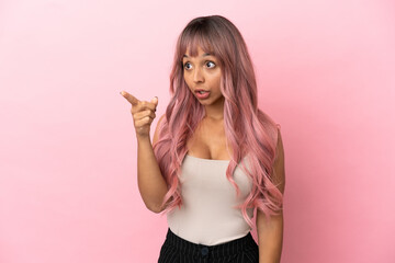 Young mixed race woman with pink hair isolated on pink background pointing away
