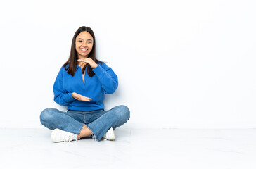 Young mixed race woman sitting on the floor isolated on white background holding copyspace...