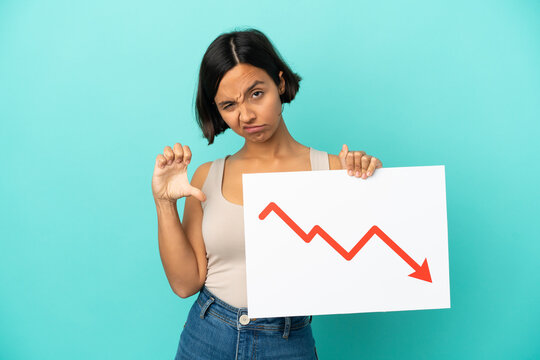 Young mixed race woman isolated on blue background holding a sign with a decreasing statistics arrow symbol and doing bad signal