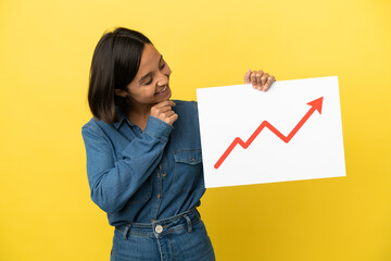 Young mixed race woman isolated on yellow background holding a sign with a growing statistics arrow...