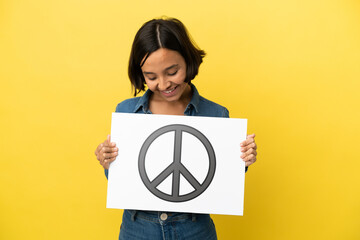 Young mixed race woman isolated on yellow background holding a placard with peace symbol