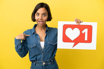 Young mixed race woman isolated on yellow background holding a placard with Like icon and pointing...