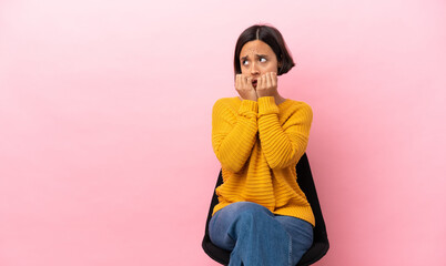 Young mixed race woman sitting on a chair isolated on pink background nervous and scared putting...