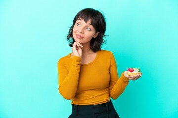 Young mixed race woman holding a tartlet isolated on blue background looking up while smiling
