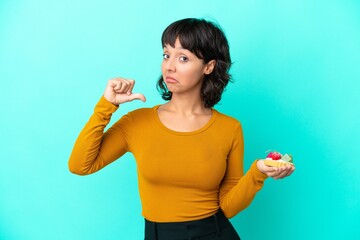 Young mixed race woman holding a tartlet isolated on blue background proud and self-satisfied
