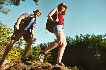 Nature, hiking and couple walking with blue sky on adventure holiday in mountain, trees, and bush. Trekking, man and woman on happy travel vacation together in woods, forest or outdoor climbing park