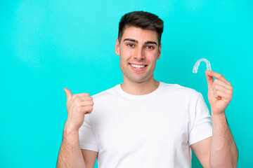 Young caucasian man wearing holding invisible braces isolated on blue background pointing to the...