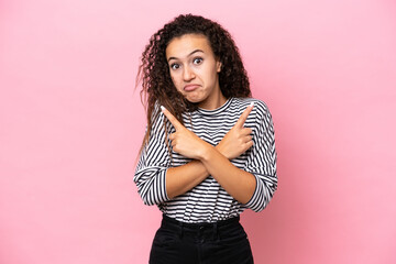 Young hispanic woman isolated on pink background pointing to the laterals having doubts