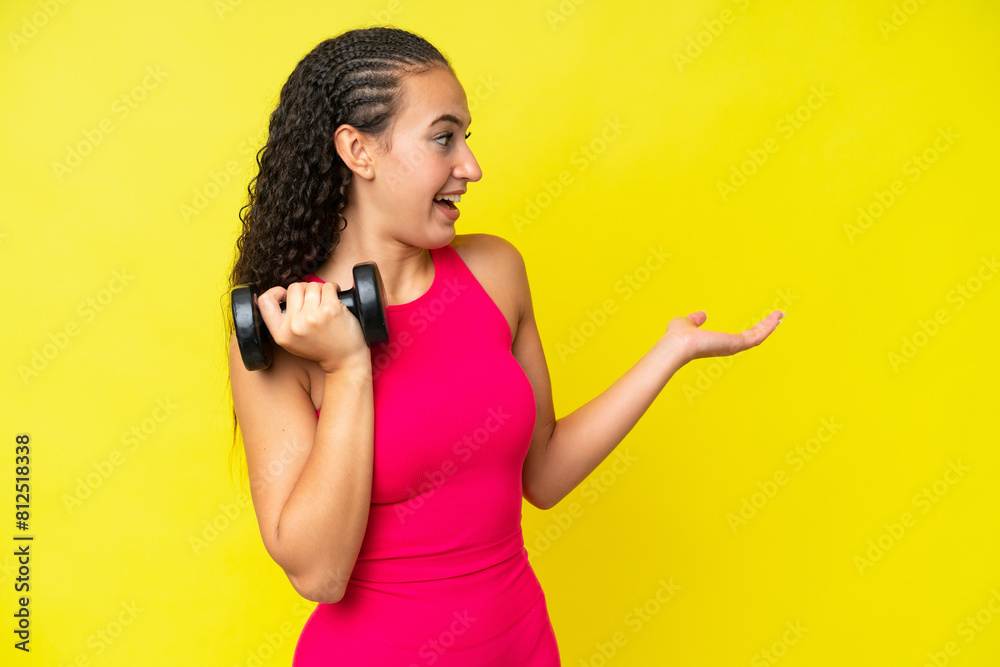 Wall mural Young sport woman making weightlifting isolated on yellow background with surprise expression while looking side