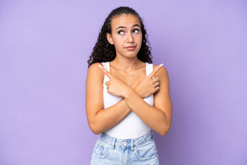Young woman isolated on purple background pointing to the laterals having doubts