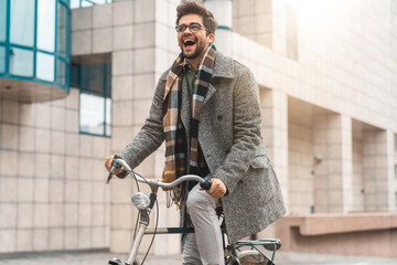 Young excited stylish businessman going to work by bike in the city.