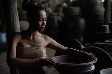 Beautiful Asian woman in traditional Thai dress holding big ceramic art pot made of pottery.
