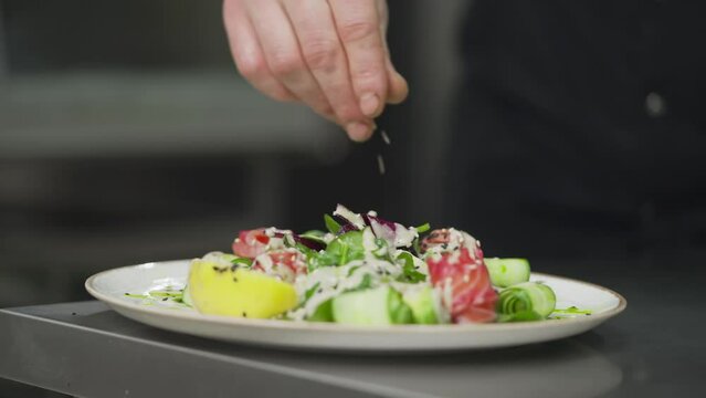 Close-up a professional chef sprinkles a prepared salad with white and black sesame seeds in the kitchen of a restaurant. A professional chef prepares the dish for serving and makes the final touches
