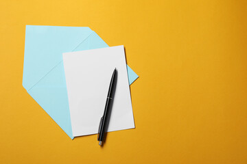 Naklejka premium Blank sheet of paper, letter envelope and pen on orange background, top view. Space for text