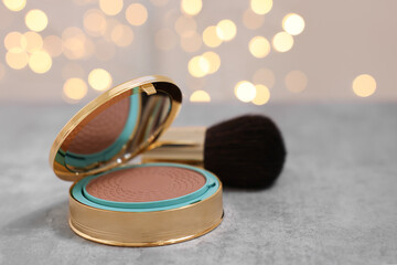Face bronzer on grey textured table against blurred lights, closeup