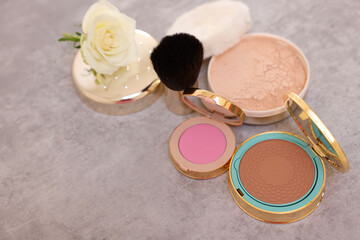 Bronzer, powder, blusher, brush and rose flower on grey textured table, above view