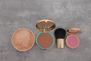 Bronzer, powder, blusher and brush on grey textured table, flat lay