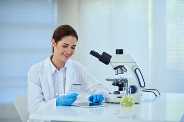Scientist, microscope and woman in office with tablet for medical exam, innovation and chemical research. Experiment, investigation and person with biotech for vaccine, study and test for bacteria