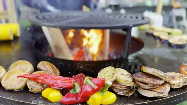 Grilled vegetables including red peppers, sliced potatoes, and yellow bell peppers, cooked on a sleek, circular outdoor grill. Ideal image for culinary presentations and outdoor cooking.