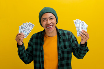 Excited Asian man in a beanie and casual clothes holds banknotes in his hand. Isolated on a bright...