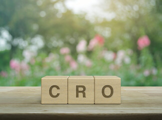 CRO acronym letter on wood block cubes on wooden table over blur pink flower and tree in park,...
