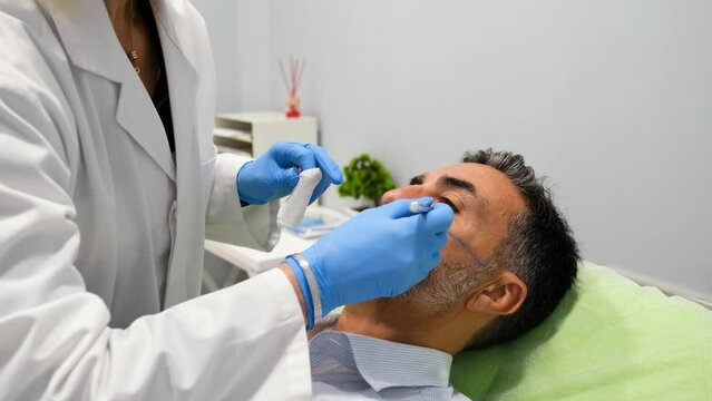 A man is getting a cheekbone filler or cheek Botox. The doctor is using a pen to draw a line on the man's cheek.