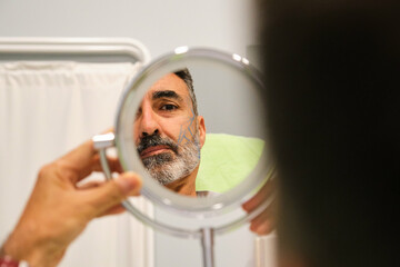 Mature Caucasian man looking into the mirror before a aesthetic treatment in a clinic.