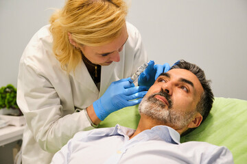 Aesthetic doctor is examining a man's face with a magnifying glass in a aesthetic clinic.