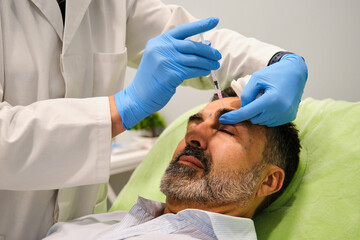 A man is getting Botox or filler for forehead wrinkles by a aesthetic doctor in a clinic.